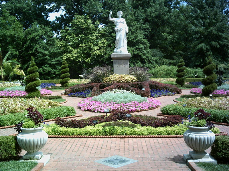 Topiary and flowers lining a brick path leading to a white statue