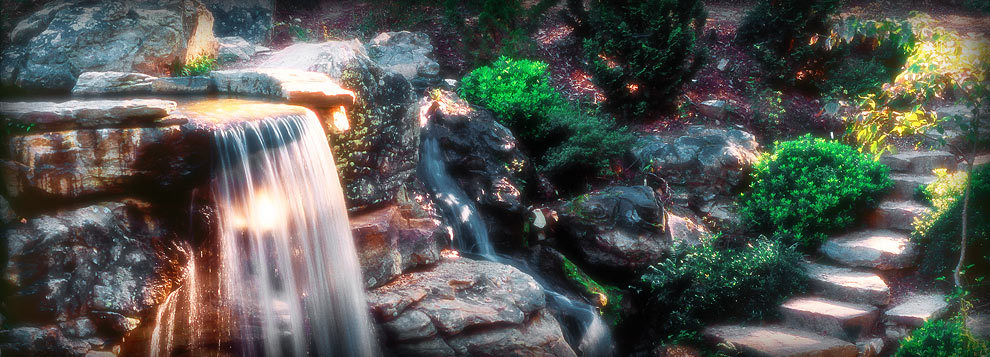 Waterfall over rocks with greenery around stone steps on the right.