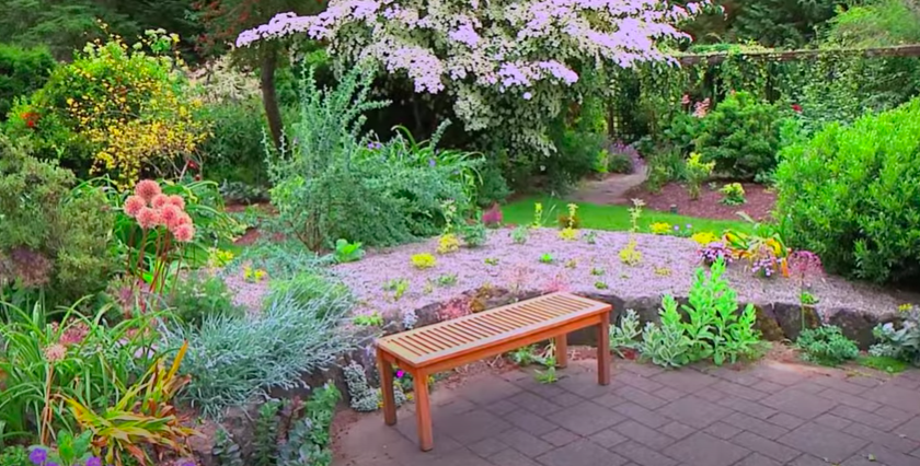Small bench in a garden with flowers all around it.