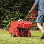 Man using gas powered aerating machine to aerate residential grass yard.