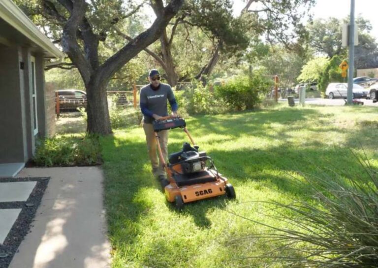 LawnStarter pro Justin Stultz uses a string trimmer to edge grass along a walkway beside a residential home.
