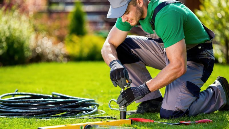 A technician inspects an irrigation system on green lawn.