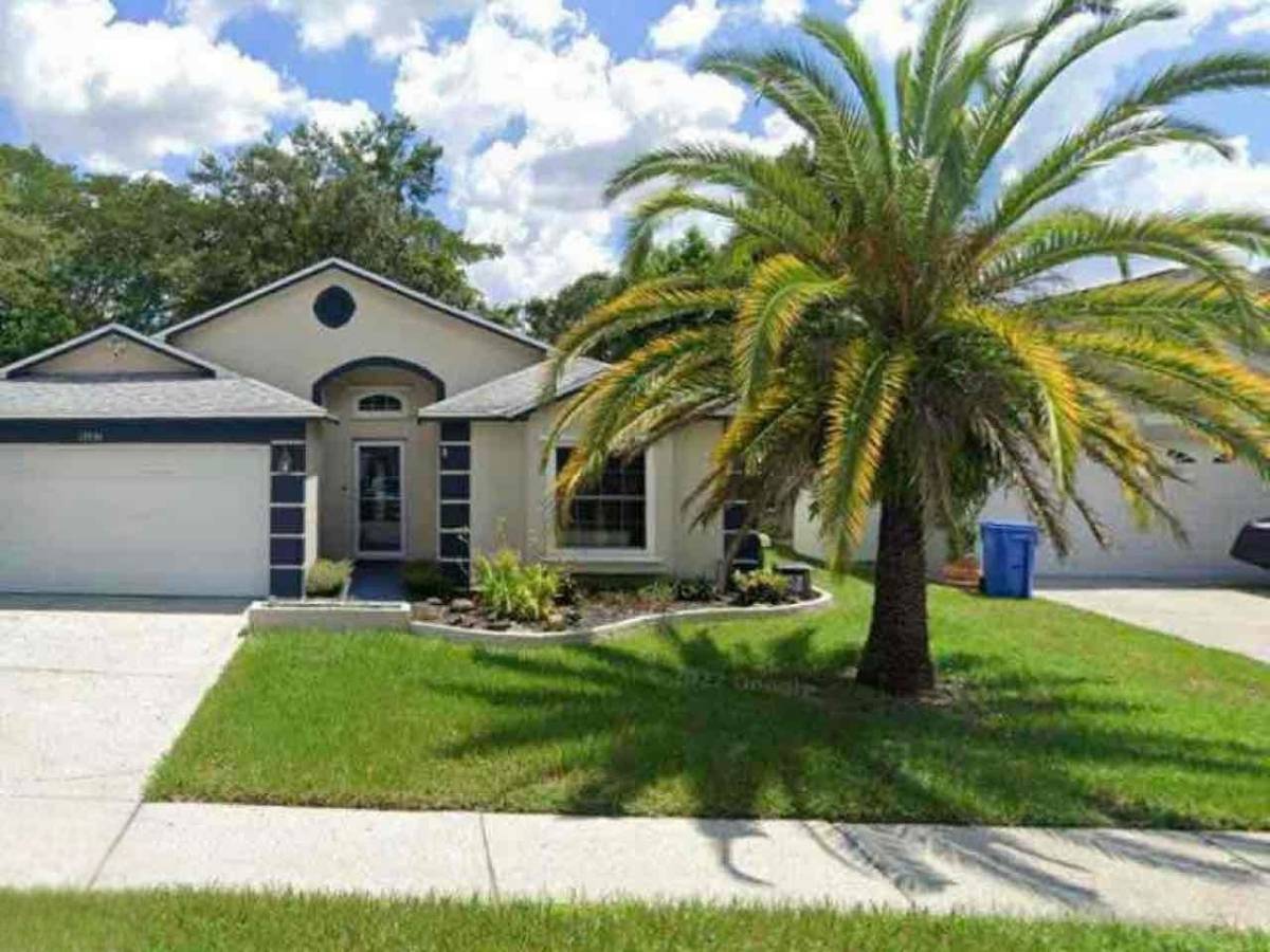 Single-story Florida home with palm tree in front yard, green lawn, driveway, garage, blue sky, and scattered white clouds.