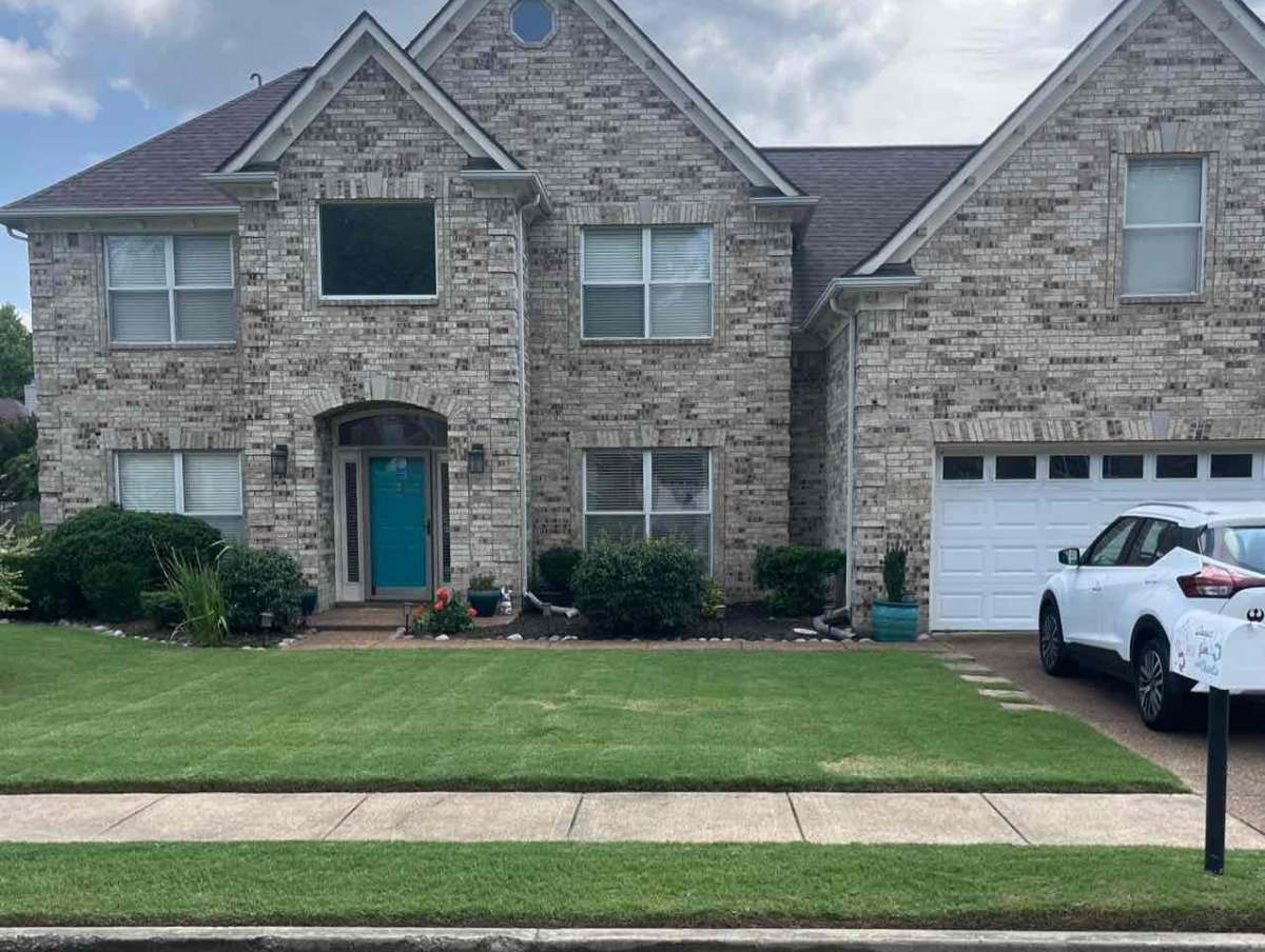 Brick two-story home with neatly mowed front lawn in Memphis, Tennessee, professionally cut by Lawnstrater Pro, driveway and car
