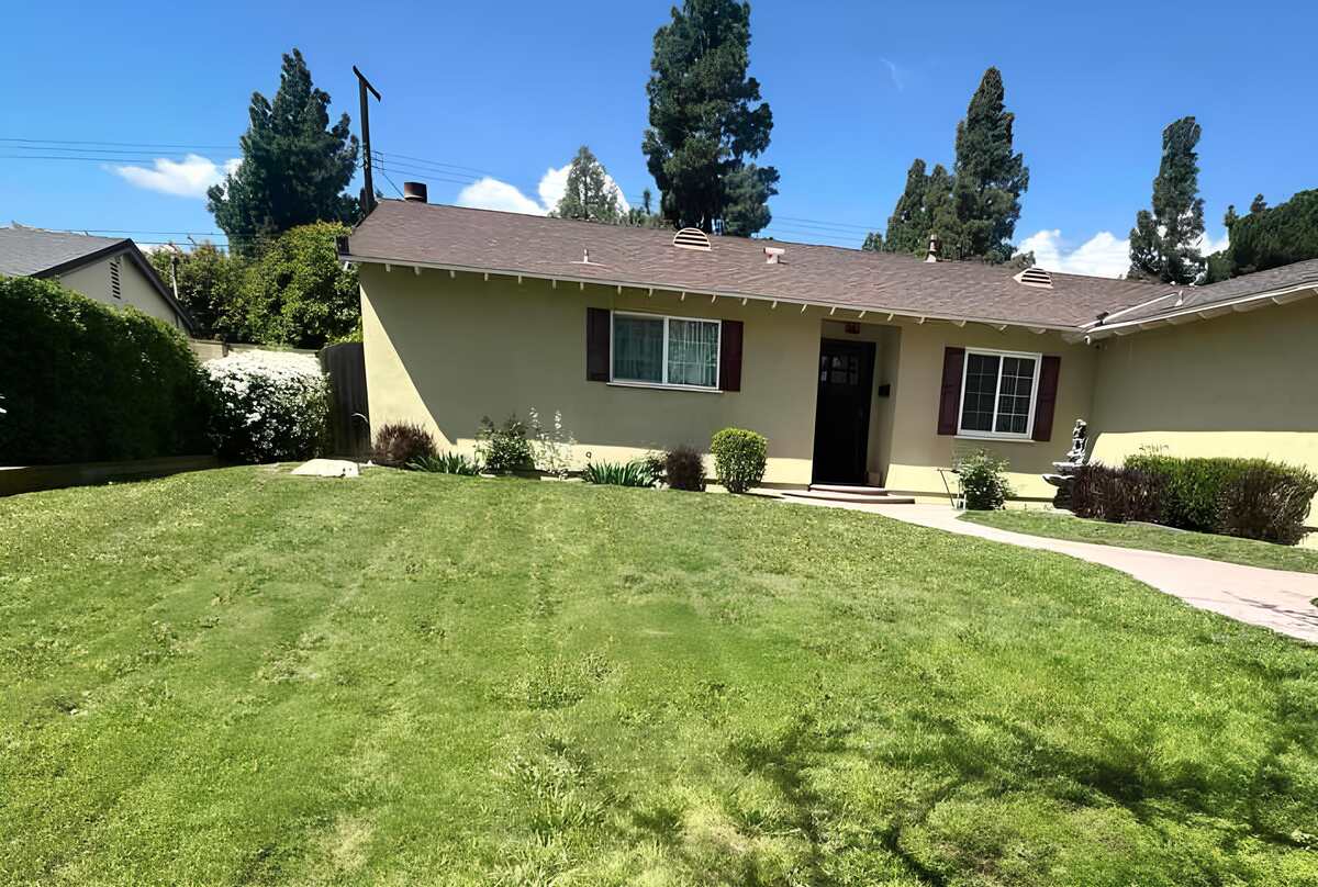 Single-story home in Los Angeles with a patchy green front lawn, shrubs along the foundation, and a concrete walkway leading to the front door.