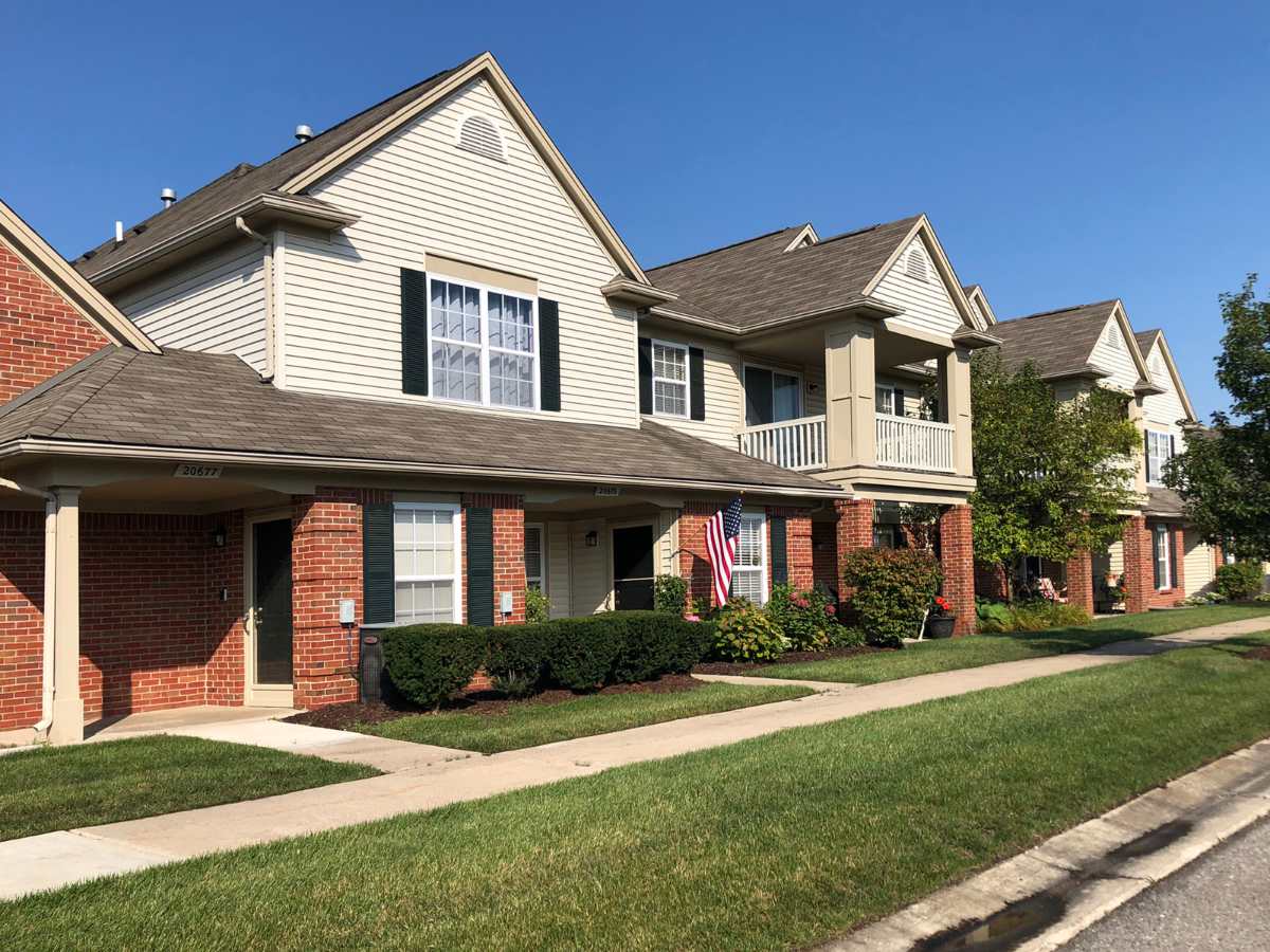 Row of condominium homes with neatly maintained green lawns in an upscale Detroit suburb under clear blue skies.
