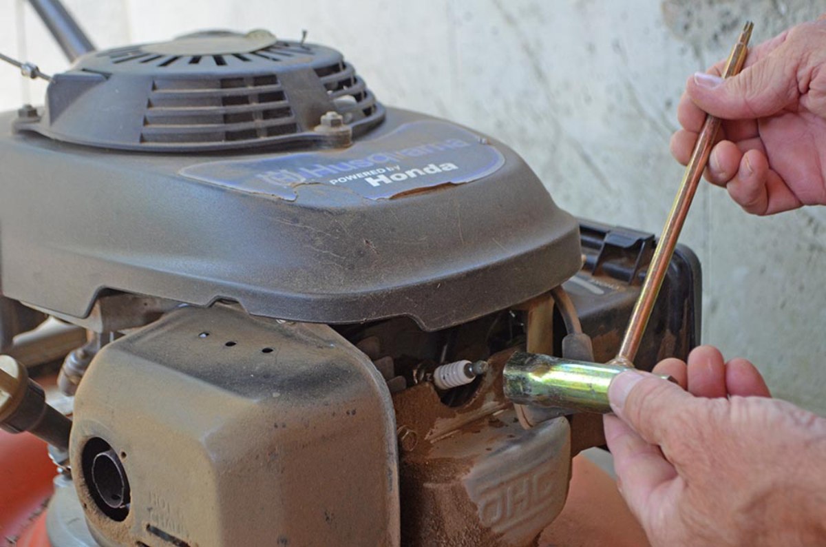 Hand using a socket wrench to remove spark plug from lawn mower engine during maintenance, ensuring reliable performance and longevity.