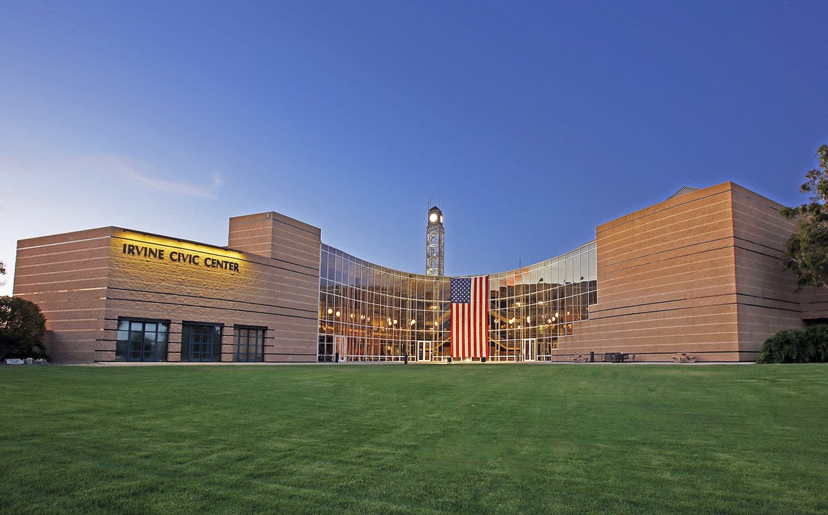 An American flag hangs down from the large windows of Irvine City Hall on a bright blue day.