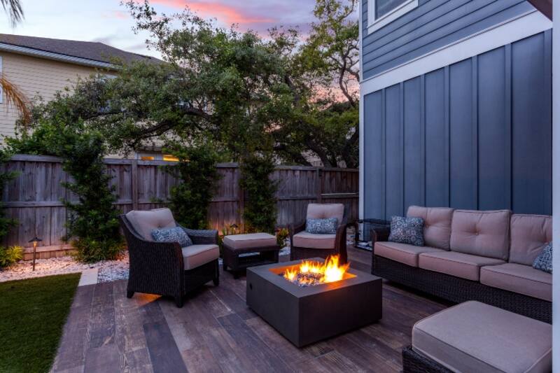 A wooden patio with a fire pit and furniture surrounded by gravel