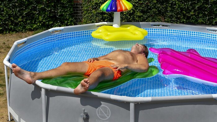 Man in swim trunks on a pool float relaxing in an above-ground pool.