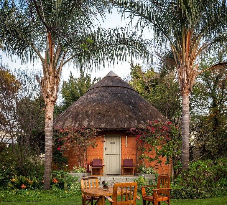 Two tall palm trees tower over a small hut near an outdoor seating area