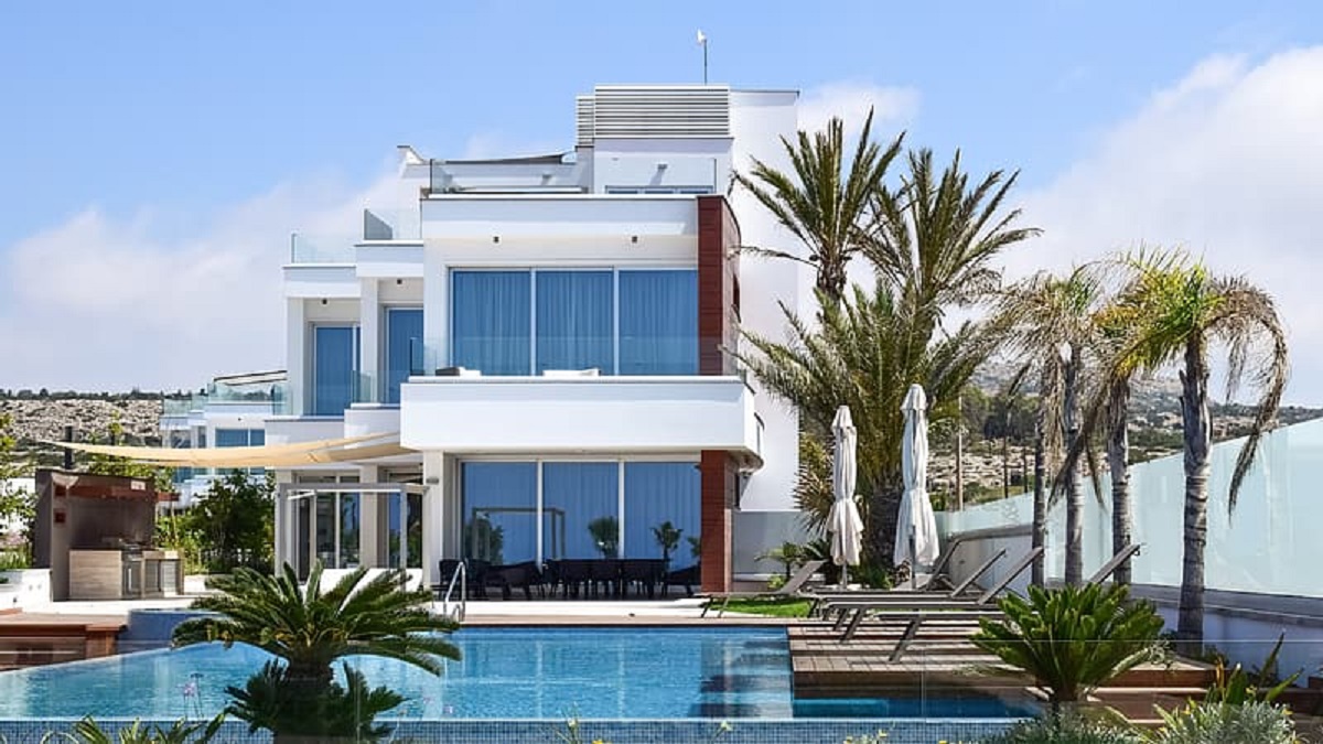 A swimming pool in front of a white house surrounded by palm trees