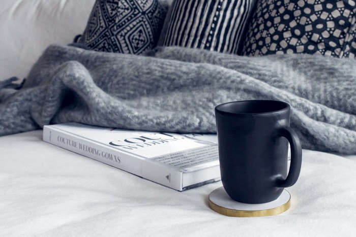 Ceramic mug on white coaster beside white book and grey blanket