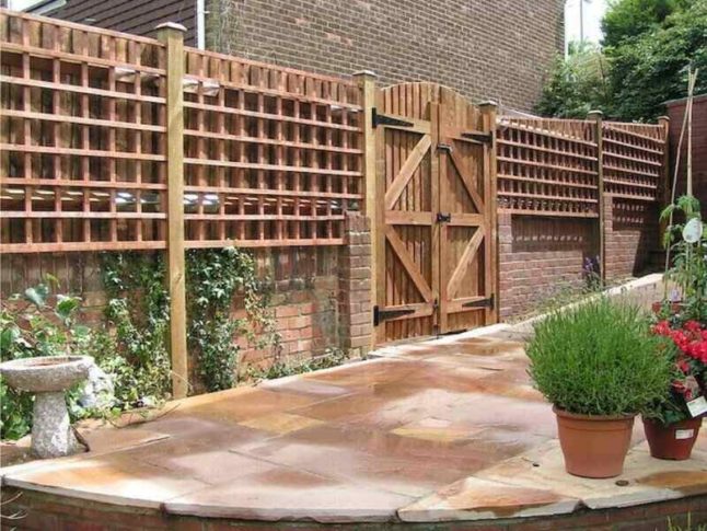 Trellis fence sits atop brick wall featuring a large wooden gate