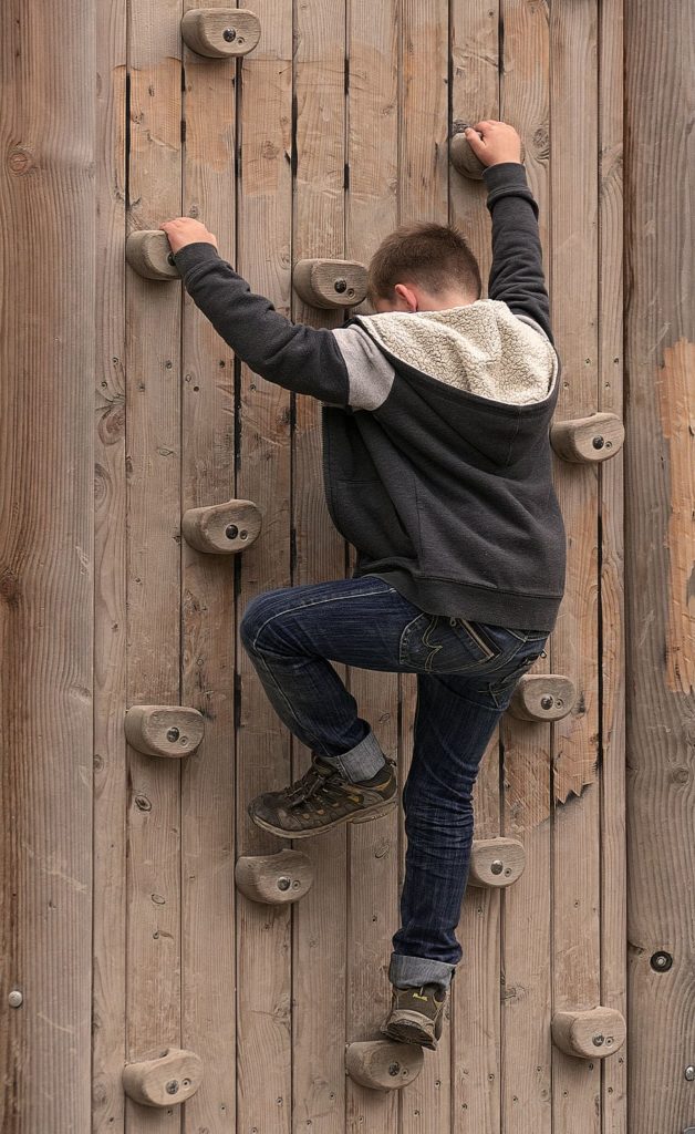 Child climbing up a wooden rock climbing wall