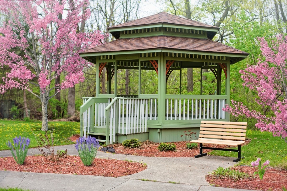 Light green, double-roofed gazebo surrounded by cherry blossom trees and other plants