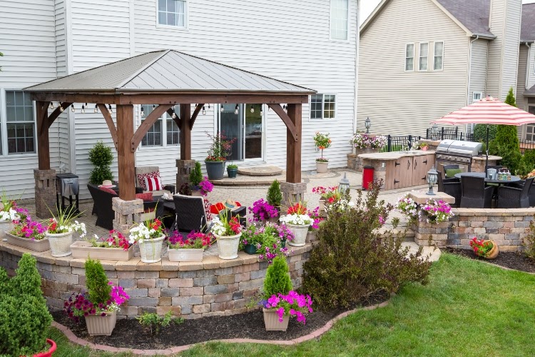 Wooden gazebo on curved patio, encircled by various potted plants