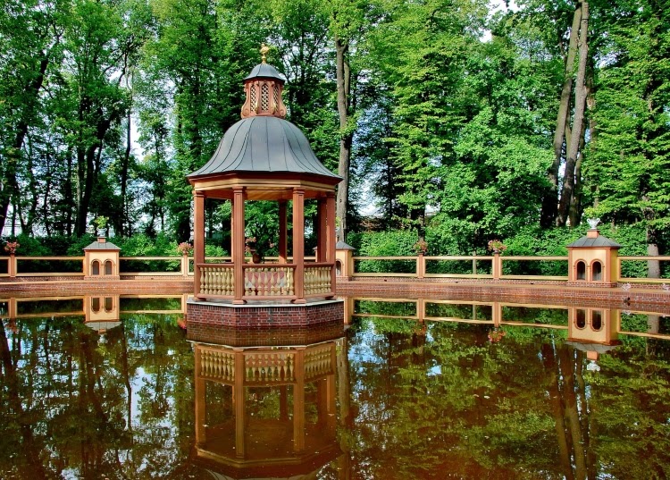 Wooden gazebo with brick foundation situated in the middle of a pond