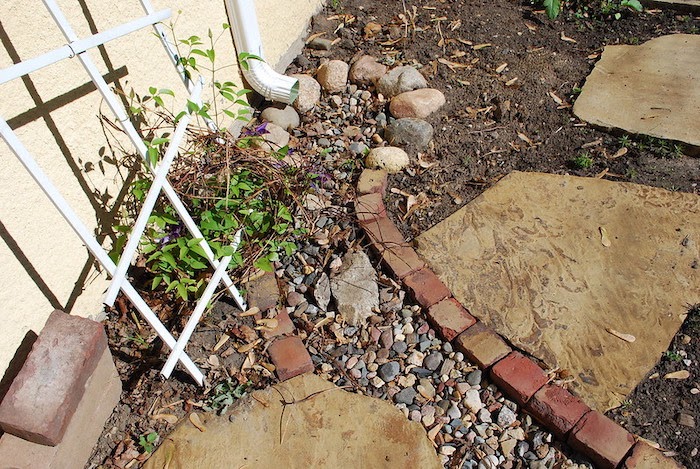 Downspout at the end of a small dry creek bed edged by brick landscaping blocks