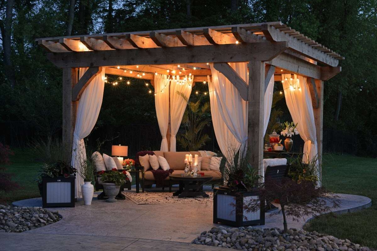 night view of wooden pergola with curtains and string lights above an island patio
