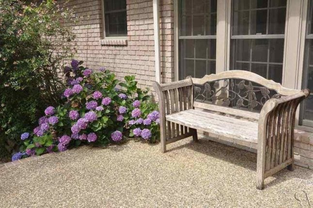 A pea gravel epoxy patio with a bench surrounded surrounded by flowers