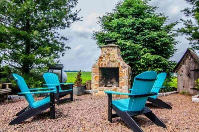 A pea gravel patio with blue chairs facing an outdoor fireplace