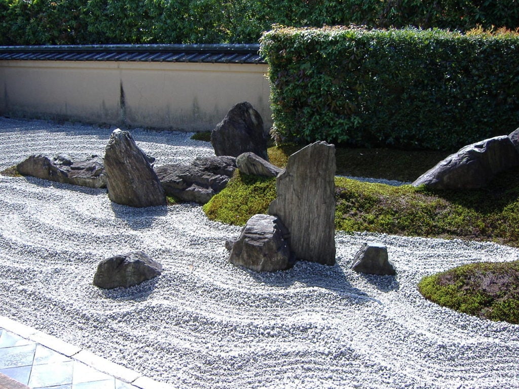 Zen garden with large vertical rocks and bushes in the background