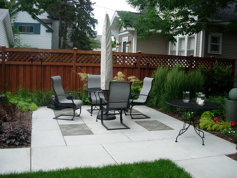 A hardscape patio made with light gray cement squares and with a patio table and umbrella