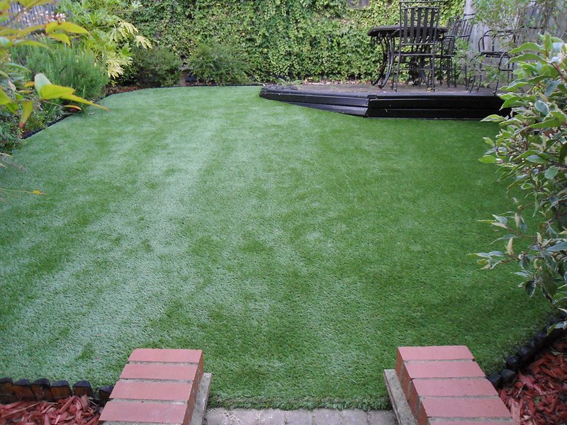 Artificial grass lawn with bushes and patio in background