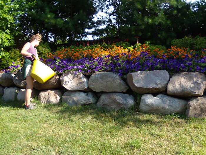 Person tends to tall flower beds supported by boulder retaining wall