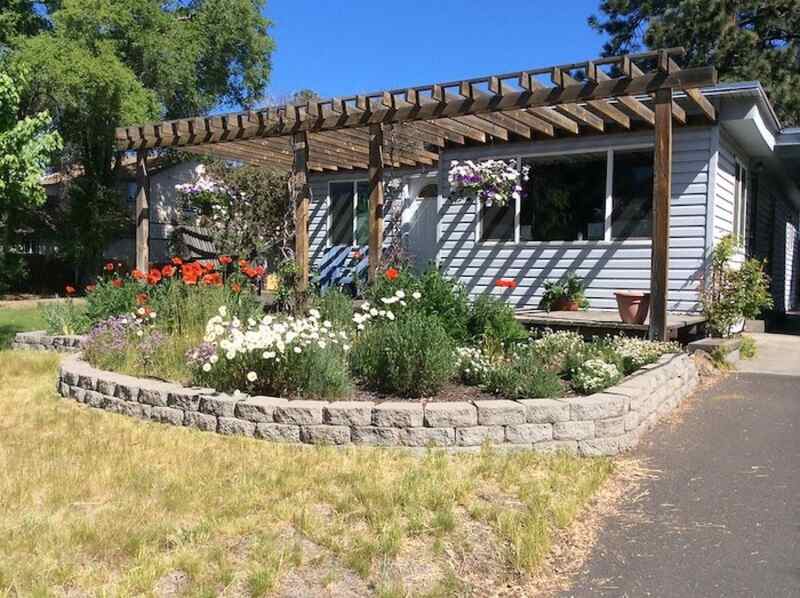 Raised flower bed with landscaping block retaining wall with pergola in background.