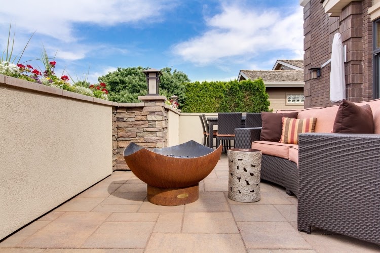 small stone patio with gray wicker sofa and curved fire pit