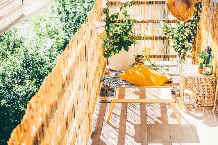 small patio with fencing adorned in floor pillows, a side table, and potted plants