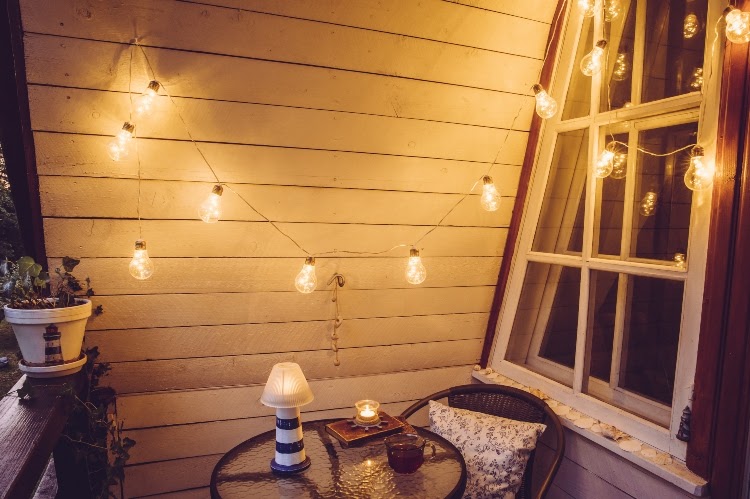small patio with white string lights, a window, and small table and chair