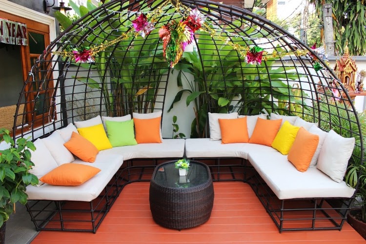 small patio with oversized lounge sofa with arched covering, hanging flowers, and a small, wicker table