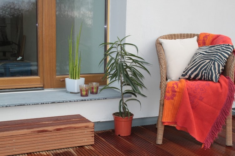small patio with wooden flooring and a wicker chair with pillows and a throw blanket