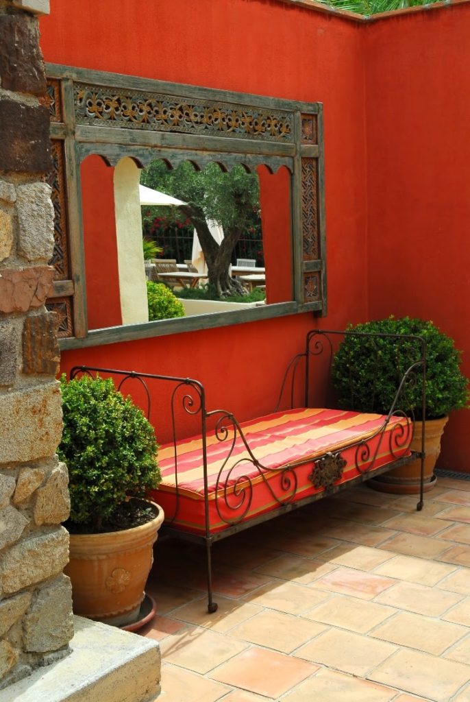 small patio with red-orange exterior walls, a framed mirror, and a cushioned bench