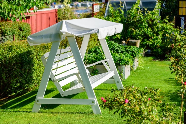 Empty white pallet swing with white canopy in green garden surroundings