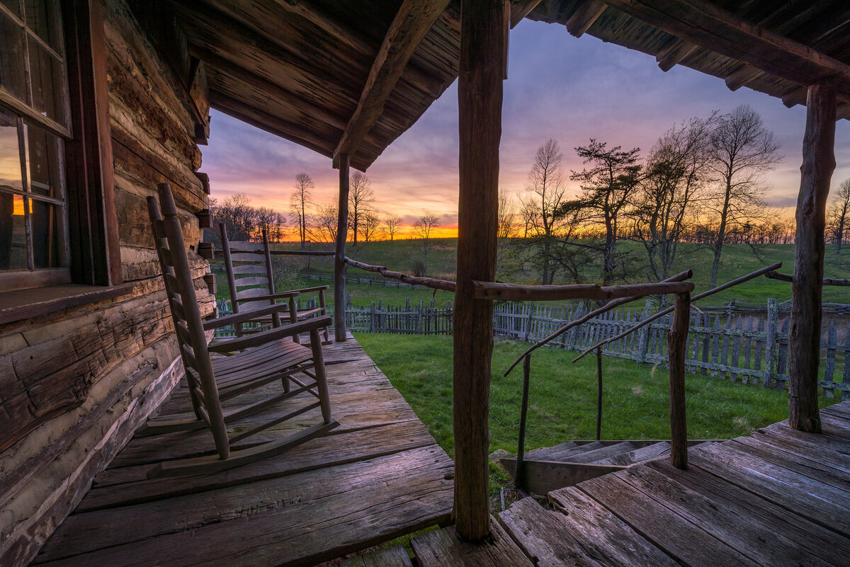 Rocking chairs on a porch of a rustic cabin with sunset off in the distance