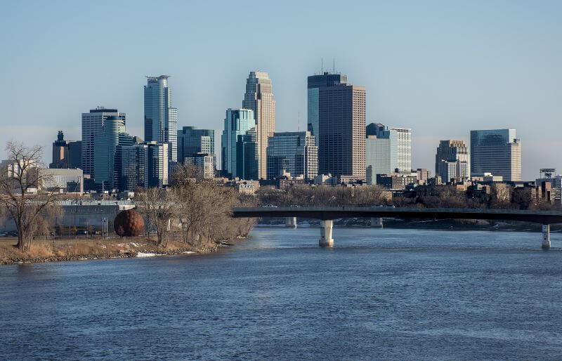 The Mississippi River rushes under a bridge in front of the Minneapolis skyline.