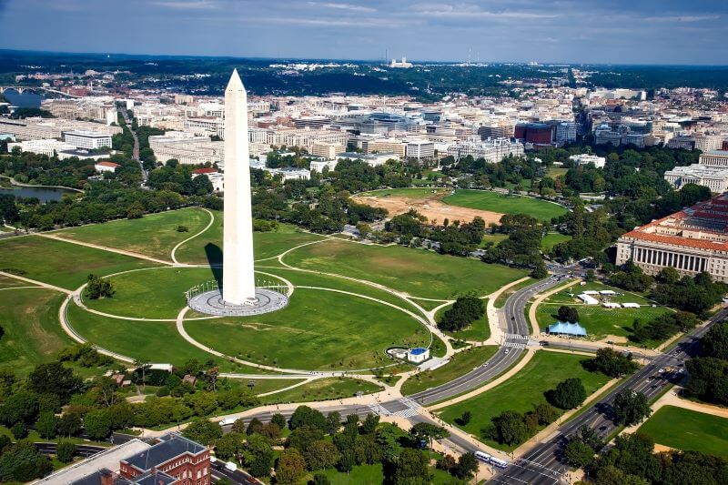 The Washington Monument stands tall above a field of grass, the White House, and the skyline of Washington, DC.