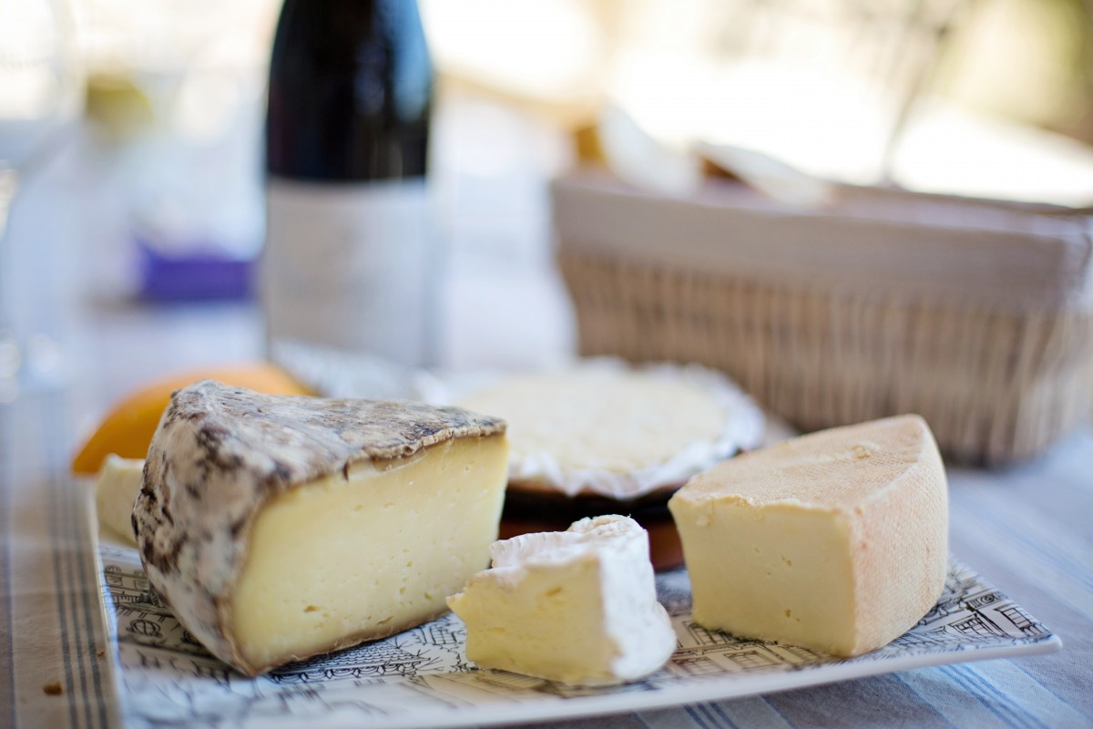 Closeup of different cheeses on a plate with wine bottle and basket in background