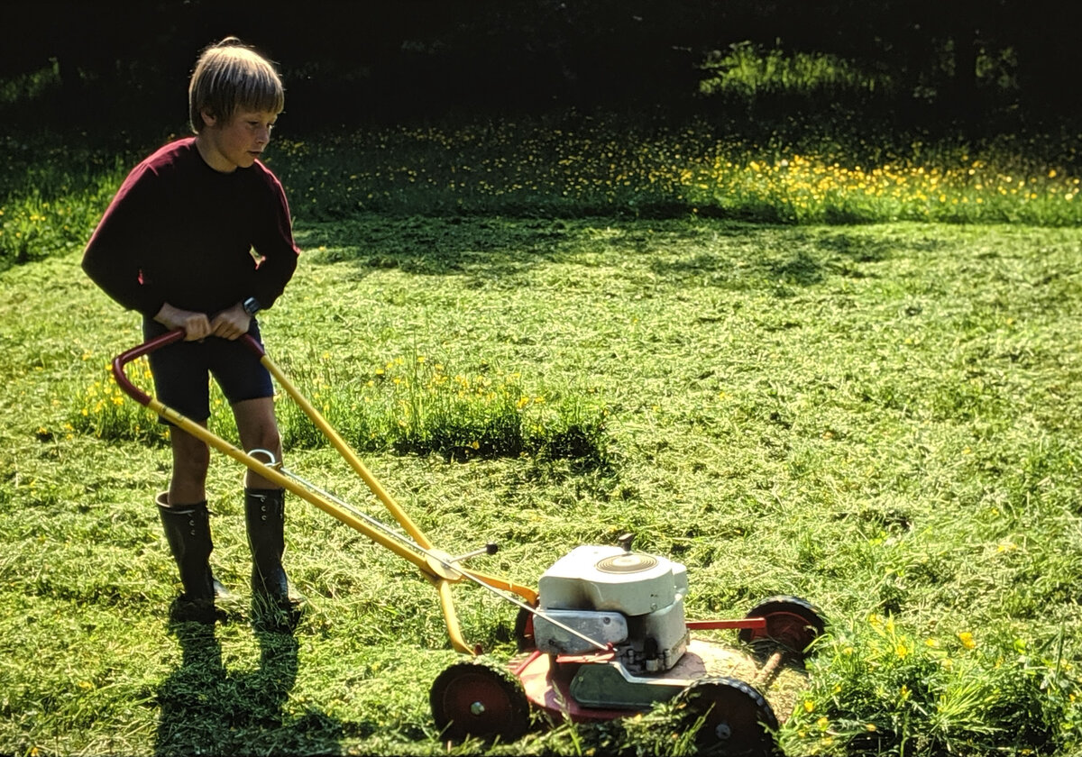 Young boy using an old fashioned mower on tall grass