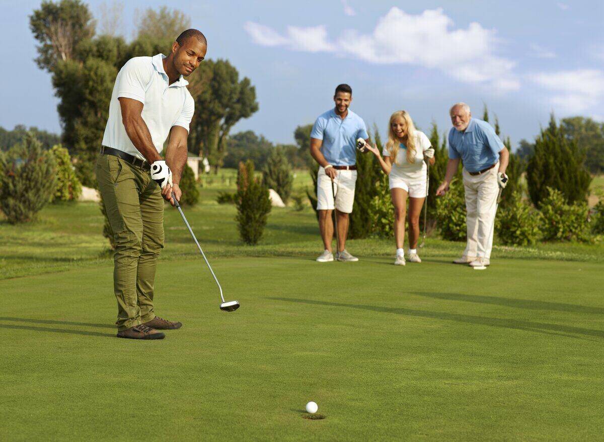 Male golfer in foreground putting in golf ball while group of two men and a woman cheer in the background