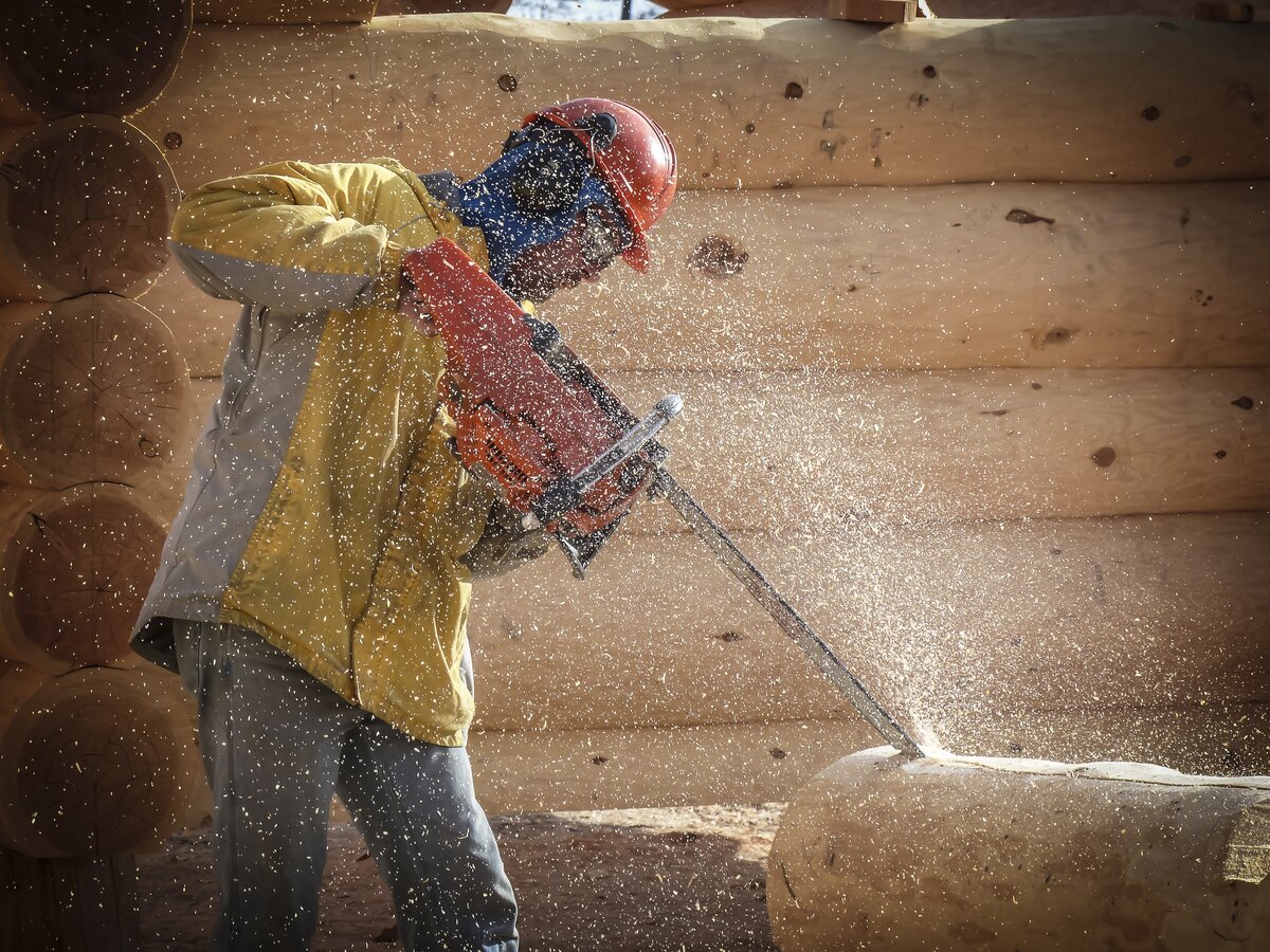 Worker cutting log with electric chainsaw