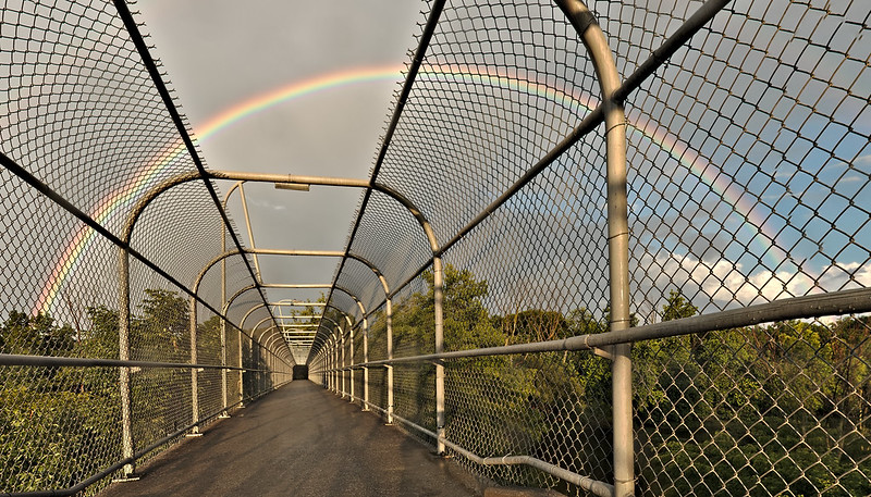 Curved chain'link fence on a bridge with a rainbow overhead