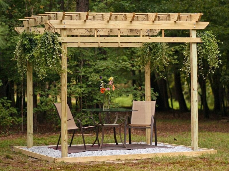 Wooden pergola with two chairs and a small table beneath it