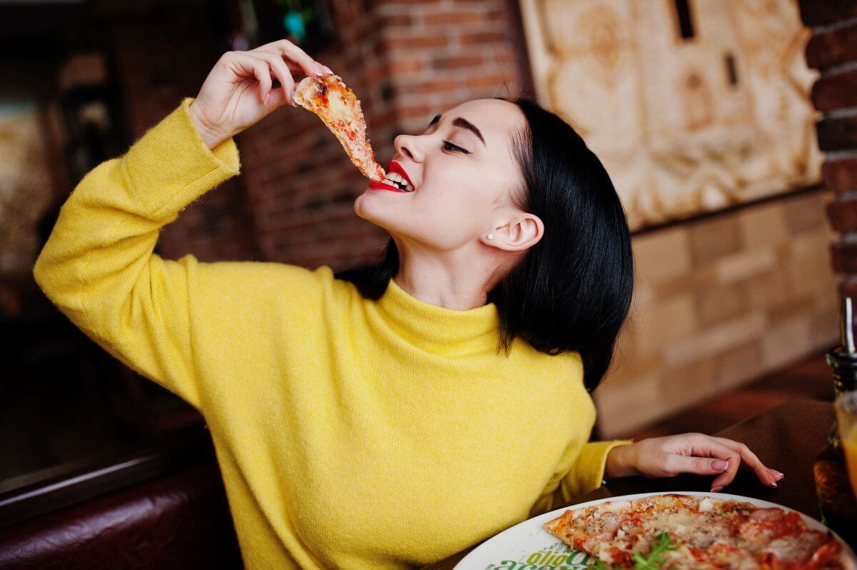 A woman enjoys a slice of cheese pizza in a restaurant