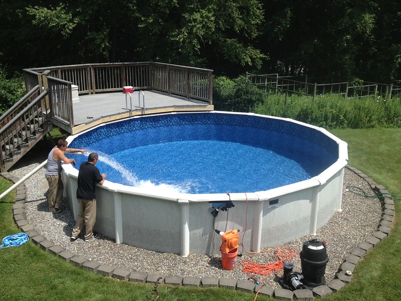 Two men filling up an above-ground pool with water