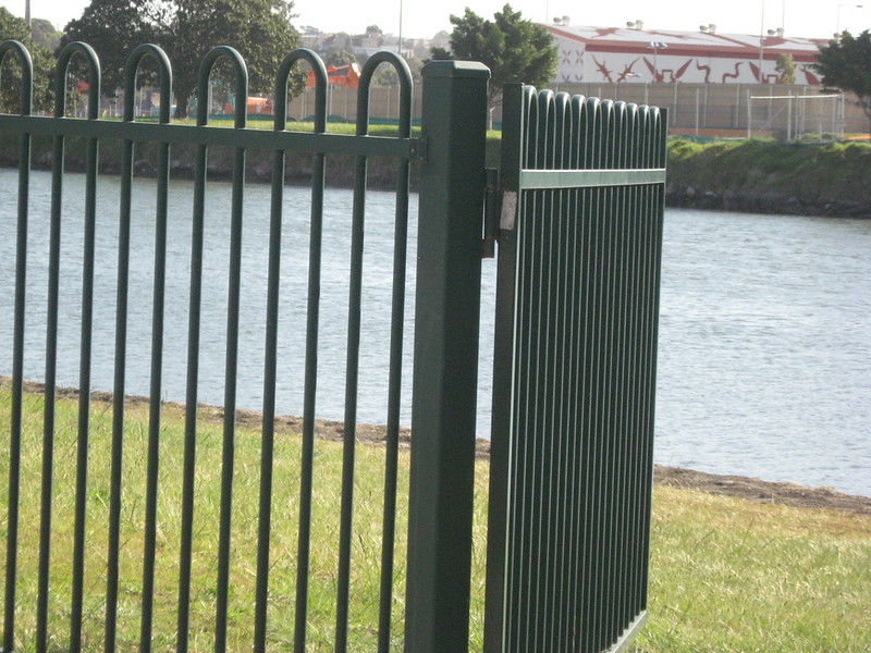 Metal fence gate open and showing a body of water beyond it